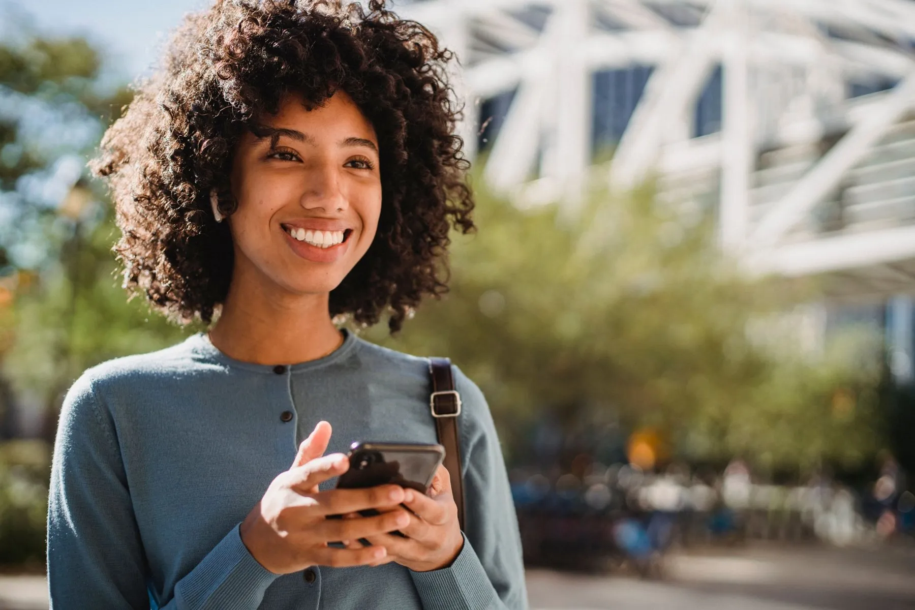 A woman smiling as she looks up from her phone outdoors